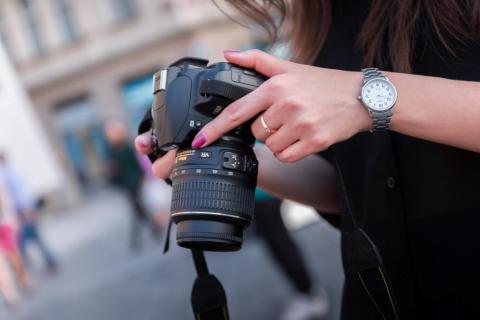 Image of a camera held downward by a person wearing a watch in front of a blurred city scene